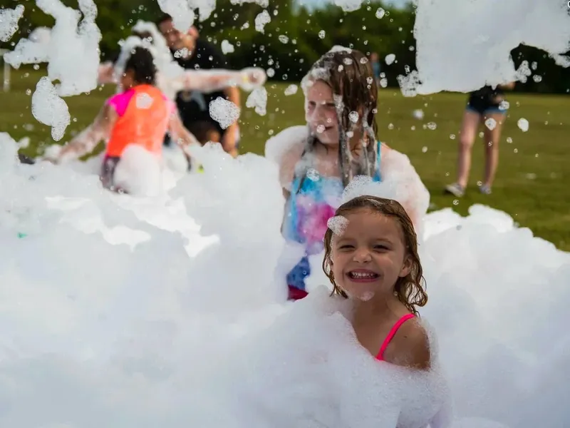 Children playing in deep white foam at an outdoor foam party.