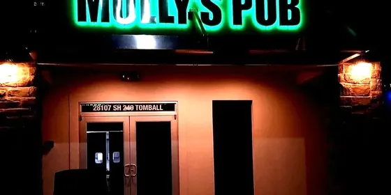 The entrance to Molly's Pub in Tomball at night, under a green neon sign.