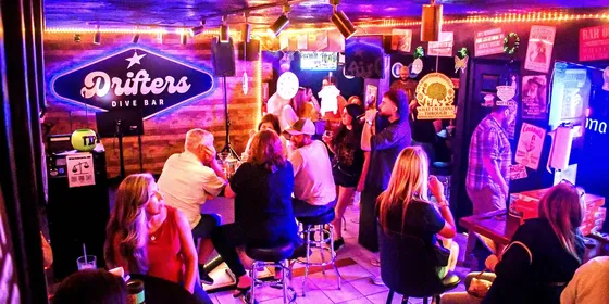 The interior of Drifters Dive Bar, guests at high tables under coloured lighting.