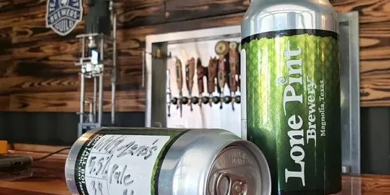 Two tall cans of Lone Pint Brewery beer standing on a bar, with taps and a painted Lone Pint Brewery wall sign behind.