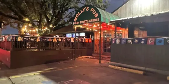The exterior and patio of Molly's Pub in The Woodlands at night, lit by strings of lights.
