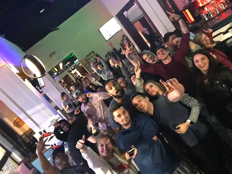 A crowded bar with guests dancing and cheering with hands raised.