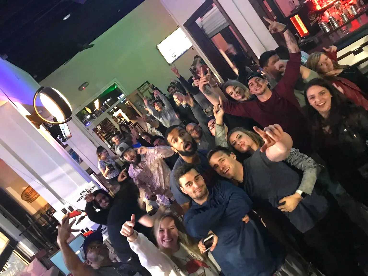 A crowded bar with guests dancing and cheering with hands raised.