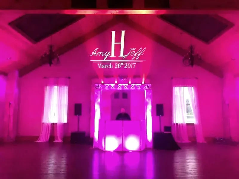 A couple's monogram projected onto the wall of a pink-uplit reception hall.