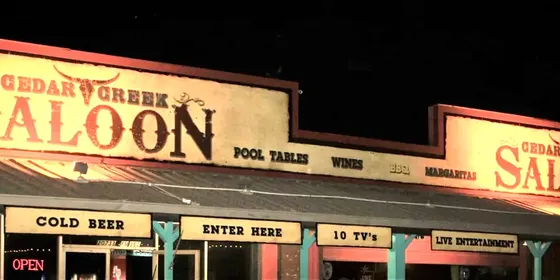 The lit frontage of Cedar Creek Saloon at night, advertising pool tables and live entertainment.