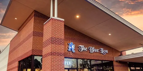 The illuminated Blue Lion sign and its blue lion emblem on a brick wall beside the entrance.