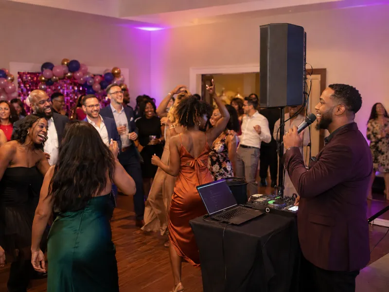 A DJ and emcee with a compact sound system leading a lively birthday dance floor.