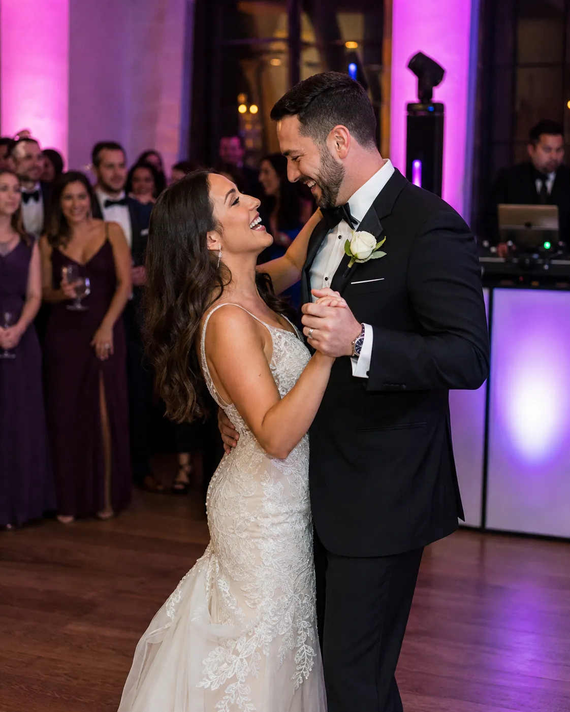 Newlyweds sharing their first dance beneath violet reception lighting as guests celebrate.